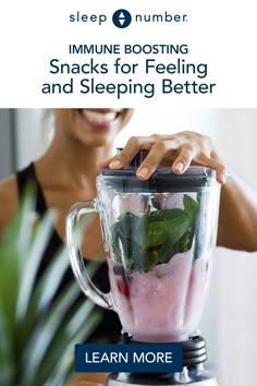 a woman smiles as she uses a blender filled with fruit and veggies