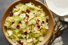 a bowl filled with cabbage and bacon on top of a table next to two plates