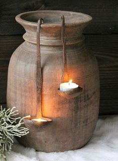 an old vase with two lit candles in it and a small plant next to it