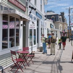 people are walking down the sidewalk in front of shops and businesses on a sunny day