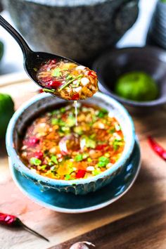 a spoon full of soup on top of a blue bowl with green peppers and limes in the background