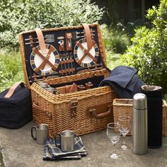 an open picnic basket sitting on top of a table next to wine glasses and other items