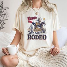 Coors Western Cowboy Shirt, Vintage 90s Graphic Western T-shirt, Rodeo Oversize Cowboy Shirt, Retro Coors Tee, Wild West Gift, Comfort Color Welcome to AuroraConceptDesign! ❤️ 👉🏻 PROCESSING TIME: - 3-5 business days. - Please contact with us if there is a rush order. 👉🏻 DELIVERY TIME: - Standard Shipping:  3-5 business days - Expedited Shipping  1-3 business days 👉🏻 CARE INSTRUCTIONS: - Machine wash cold and tumble dry low.  - Do not iron directly onto the design. - Do not bleach. We offer wide variety of products, including Unisex T-shirts, Women's V-neck T-shirts, Unisex Long Sleeve T-shirts, Youth T-shirts, Toddler T-shirts, and many more. Swipe listing images and check all the colors available for each type of shirt. Please enter the shirt and text color desired for your shirt in Coors Cowboy, Cowboy Baby Clothes, Coors Rodeo, 90s Cowboy, Baby Cowgirl, Rodeo Gifts, Cowgirl Baby, Cowboy Baby, Rodeo Shirts