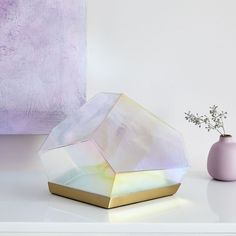 a white vase sitting on top of a table next to a purple vase with flowers in it