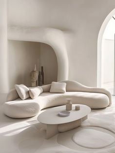 a living room filled with white furniture next to an arch shaped wall and flooring