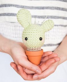 a person holding a small crocheted animal in a cup with an orange cone