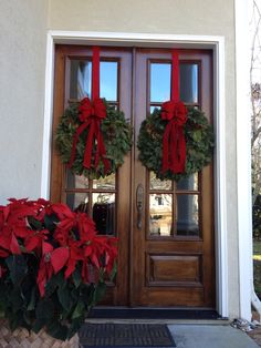 two christmas wreaths on the front door of a house with red bows and poinsettias