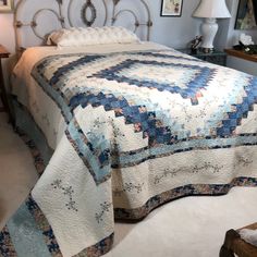 a bed with a blue and white quilt on it's headboard in a bedroom