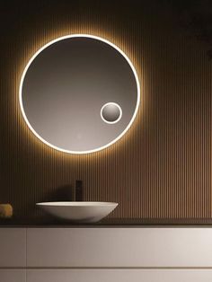 a white sink sitting under a round mirror in a bathroom next to a wooden wall