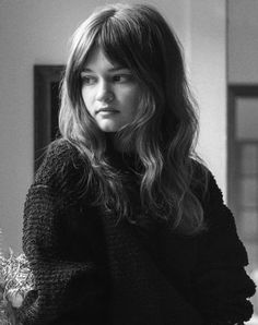 a black and white photo of a woman with long hair sitting on a couch next to a vase