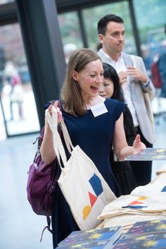 a woman is laughing as she looks at books on a table with other people in the background