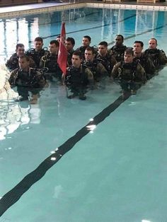 a group of men in scuba suits sitting on the side of a swimming pool next to each other