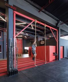 a woman is hanging upside down on a rope in an empty gym with red walls