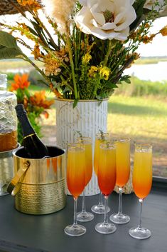 four champagne flutes are lined up on a table with flowers in vases and wine glasses