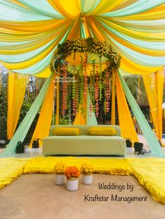 an outdoor wedding setup with yellow and green draping on the ceiling, white vases filled with flowers