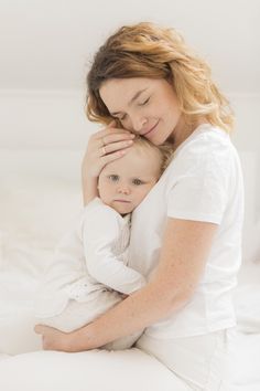 a woman holding a baby in her arms on top of a white sheeted bed