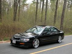 a black car is parked on the side of the road in front of some trees