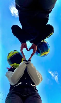 two people making a heart shape with their hands while standing in front of a blue sky