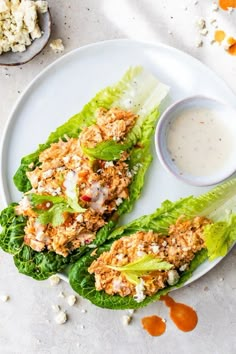 two lettuce wraps on a white plate with dressing in a bowl next to them