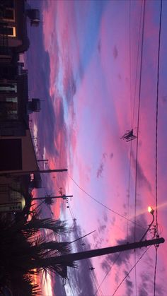 the sky is pink and blue as it sets in front of some buildings with palm trees