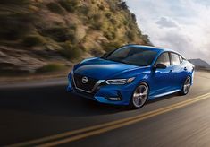 a blue nissan car driving down the road with mountains in the backgrouund