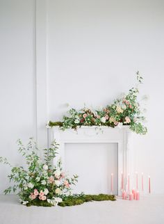 a white fireplace with candles and flowers on it