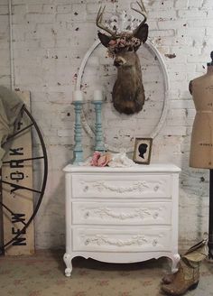 a white dresser with a deer head mounted on it's wall next to mannequins