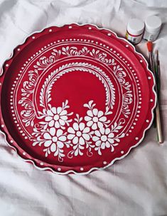 a red plate with white flowers on it next to paintbrushes and watercolors