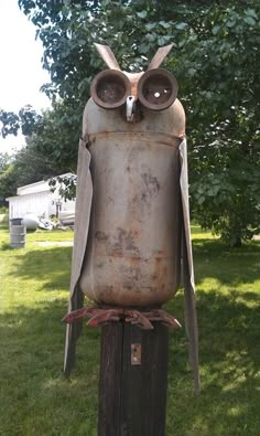 an old metal owl statue sitting on top of a wooden post in the grass next to a tree