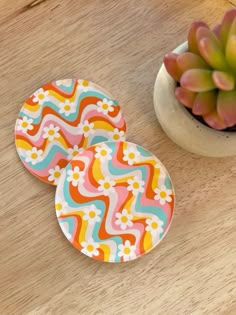 two coasters sitting on top of a wooden table next to a potted plant