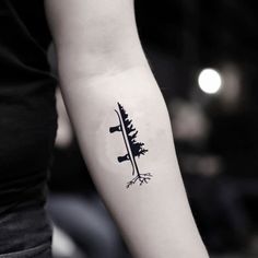 a person with a tattoo on their arm holding a knife and pine tree in the background