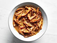 a white bowl filled with meat and sauce on top of a marble countertop next to a spoon