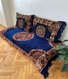 a bed with blue and red bedspread on wooden floor next to potted plant