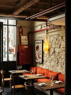 an empty restaurant with wooden tables and orange booths in front of a brick wall that has been painted red