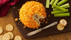 a cheese ball with celery sticks and crackers on a wooden cutting board