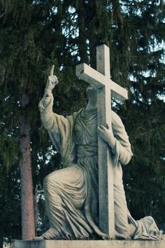 a statue of jesus holding a cross in front of some trees