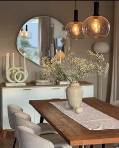 a wooden table topped with a vase filled with flowers next to two lights hanging from the ceiling