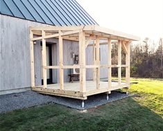 a small wooden structure sitting on top of a grass covered field next to a building