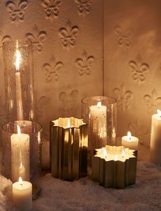 several candles are lit in front of a wall with fleur de lis on it