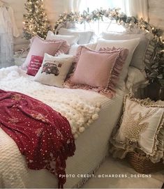 a white bed topped with lots of pillows and blankets next to a fire place filled with christmas lights