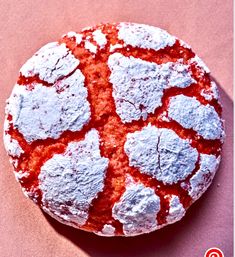 a round pastry with powdered sugar on top sits on a pink surface next to a spoon