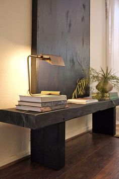 a wooden table topped with books next to a lamp on top of a hard wood floor