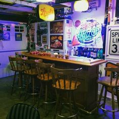 a bar with several stools in front of it and neon signs on the wall