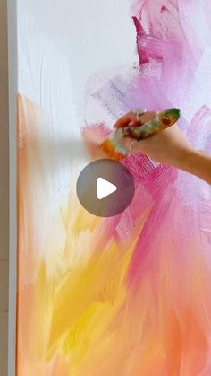 someone is painting a large piece of art on the wall with pink and yellow paint