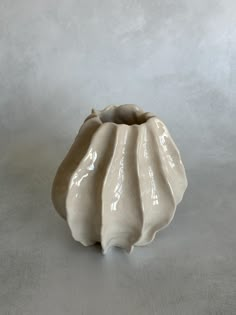 a white ceramic vase sitting on top of a table next to a gray wall and floor