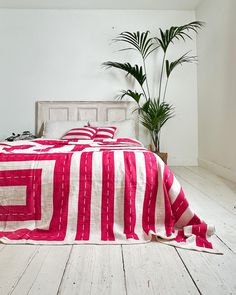 a bed covered in a red and white striped blanket next to a potted plant