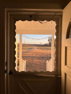 an open door with a view of a field through the window and trees in the distance