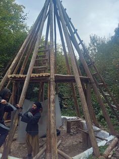 two people standing in front of a building made out of wood sticks and logs,