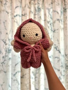 a hand holding a small crocheted doll with a pink scarf around it's neck