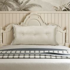 a bed with white sheets and pillows in a room that has palm trees on the wall